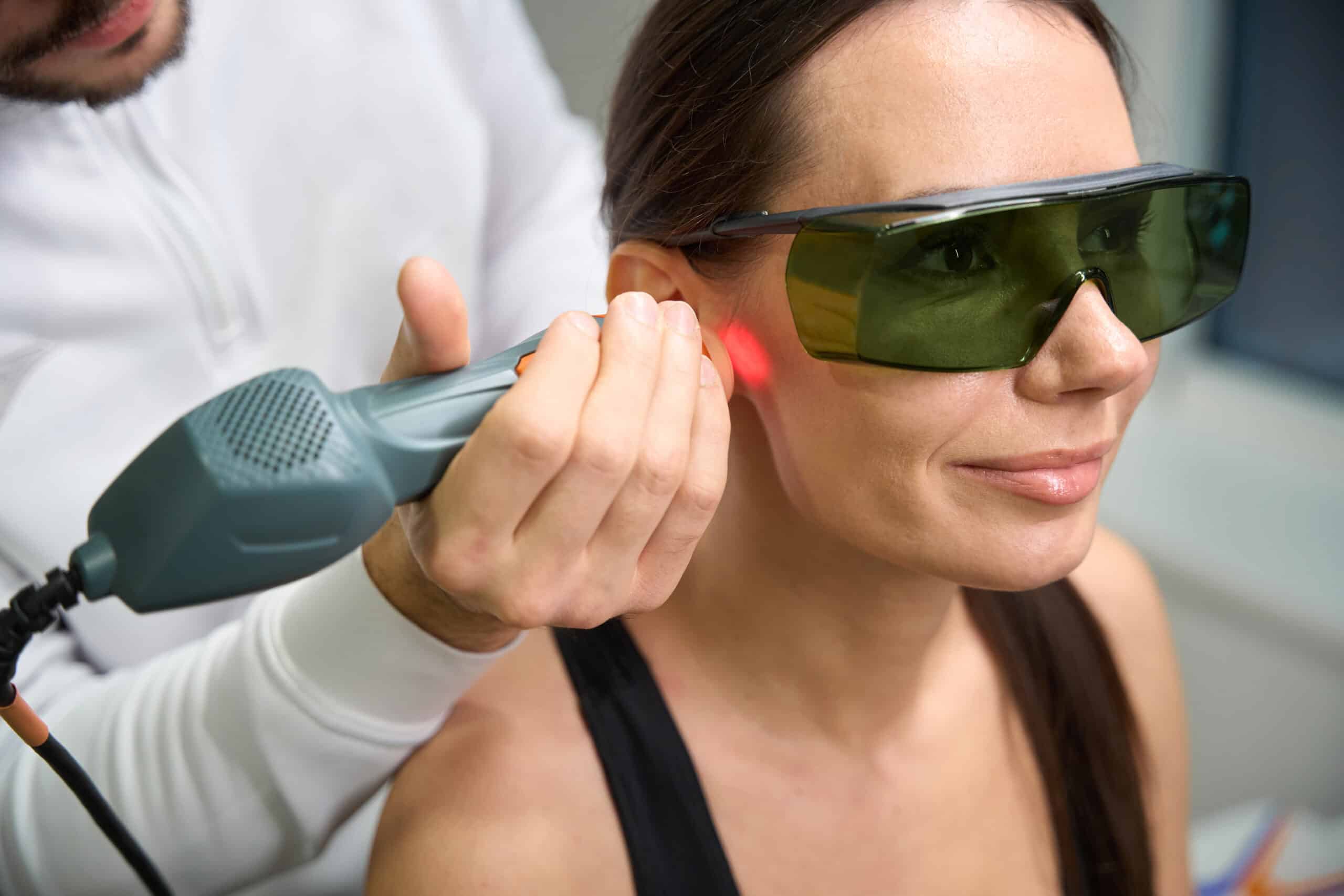 Close up photo of female in protective glasses undergoing laser therapy for reduction of swelling and inflammation on face
