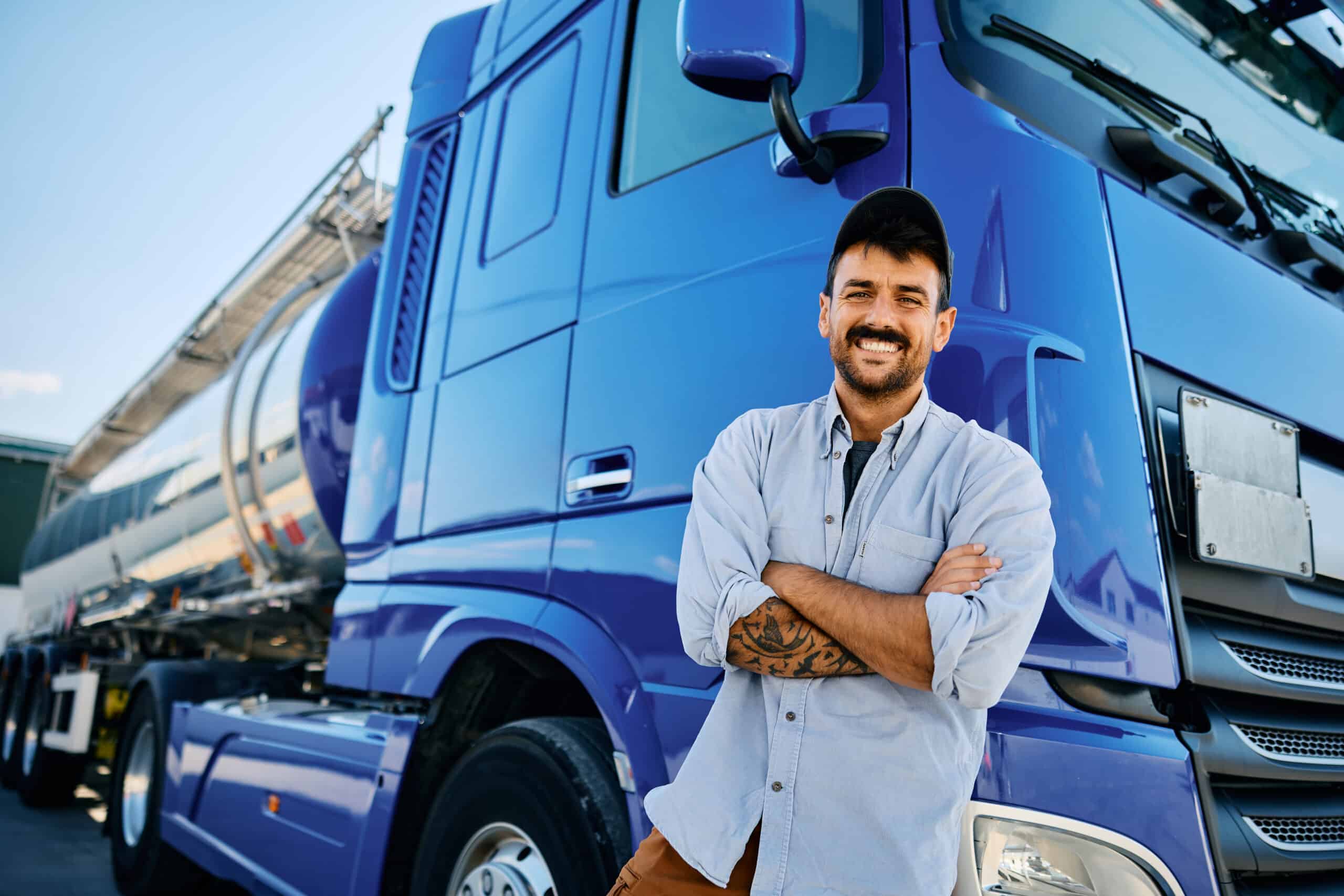 Confident truck driver leaning on his vehicle and looking at camera.